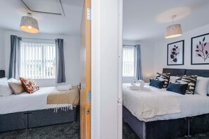A hotel room with two beds, a window with curtains, a wall-mounted light fixture, and framed artwork. - Stylish 2 BDR APT Free Parking Liverpool (Liverpool)