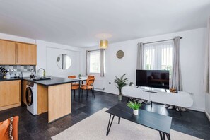 Eine moderne Küche mit Waschmaschine, Essbereich mit Stühlen, einem Fernseher und einem weißen Sofa.