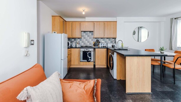 Una cocina moderna con armarios de madera, una isla central y un comedor con sillas color naranja.