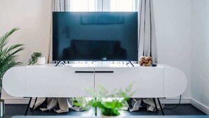 Un salón moderno con televisor de pantalla plana, mueble blanco de entretenimiento y una planta en maceta.