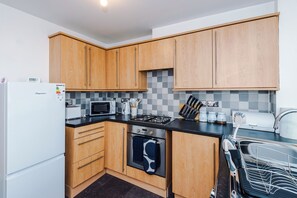 A compact kitchen with wooden cabinets, a microwave, a stove, and a dishwasher. - Stylish 2 BDR APT Free Parking Liverpool (Liverpool)