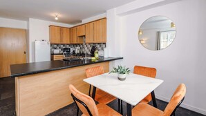 Una cocina moderna con armarios de madera, encimera negra y una mesa de comedor blanca con sillas anaranjadas.