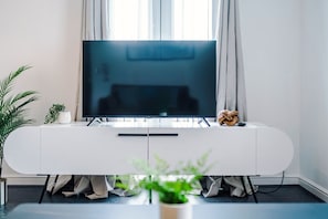 A modern living room with a flat-screen TV on a white console, a potted plant, and a decorative wooden knot. - Stylish 2 BDR APT Free Parking Liverpool (Liverpool)