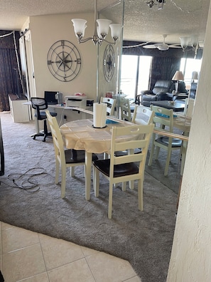 Uma sala de jantar com uma mesa redonda, cadeiras, um candelabro e um espelho grande que reflete o ambiente.