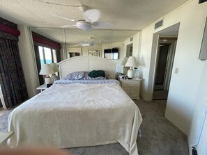 Quarto de hotel com cama, mesa de cabeceira, luminária, ventilador de teto e espelho.