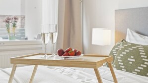 A bed with white bedding, a bedside lamp, and a tray with two glasses of water and strawberries. - Home Spa | Balcony | EV Parking | 200m Tram | 3BR (Helsinki)