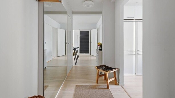 A modern interior with a wooden chair, a dining table, and a large mirror reflecting the hallway. - Home Spa | Balcony | EV Parking | 200m Tram | 3BR (Helsinki)
