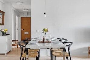 A dining area with a white table set for six, black chairs, a vase with flowers, and a pendant light. - Home Spa | Balcony | EV Parking | 200m Tram | 3BR (Helsinki)