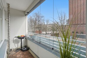 A balcony with a view of a brick building, a metal pole, and a small table with fruits. - Home Spa | Balcony | EV Parking | 200m Tram | 3BR (Helsinki)