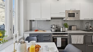 A modern kitchen with white cabinets, a microwave, an oven, and a dining area with breakfast items. - Home Spa | Balcony | EV Parking | 200m Tram | 3BR (Helsinki)