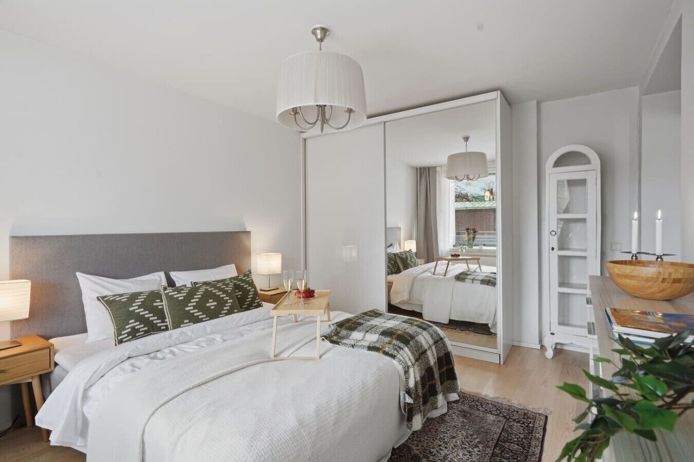 A modern bedroom with a large bed, bedside tables, a mirror, and a wooden bowl on a side table.