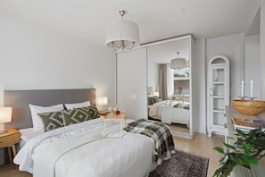 A modern bedroom with a large bed, bedside tables, a mirror, and a wooden bowl on a side table. - Home Spa | Balcony | EV Parking | 200m Tram | 3BR (Helsinki)