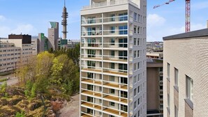 Un edificio moderno de varios pisos con balcones, una grúa de construcción y otros edificios al fondo.