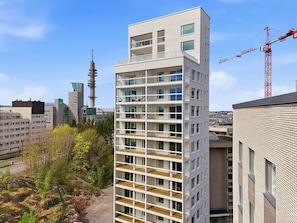 Ein modernes, mehrstöckiges Gebäude mit Balkonen, einem Baukran und weiteren Gebäuden im Hintergrund.