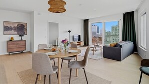 Una sala de estar moderna con comedor, un sofá, un televisor y un gran ventanal con cortinas.