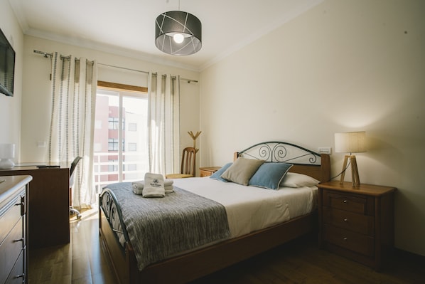 Ein Schlafzimmer mit einem Bett, Nachttischen, einer Lampe, einem Schreibtisch und einem Sessel.