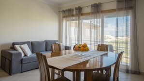 Un comedor con mesa de madera, sillas, un bol de fruta y un sofá gris.