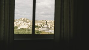 Vista desde una ventana a un paisaje desértico con una estatua.