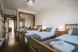 Ein Hotelzimmer mit drei Betten, hölzernen Kopfteilen, Nachttischen mit Lampen, einem großen Spiegel und einem Holzboden.