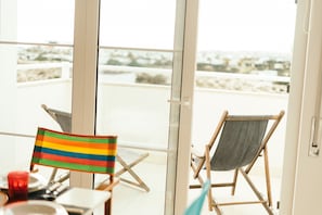 Ein Balkon mit zwei Klappsesseln, einem Tisch mit einem Glas und einer Flagge.