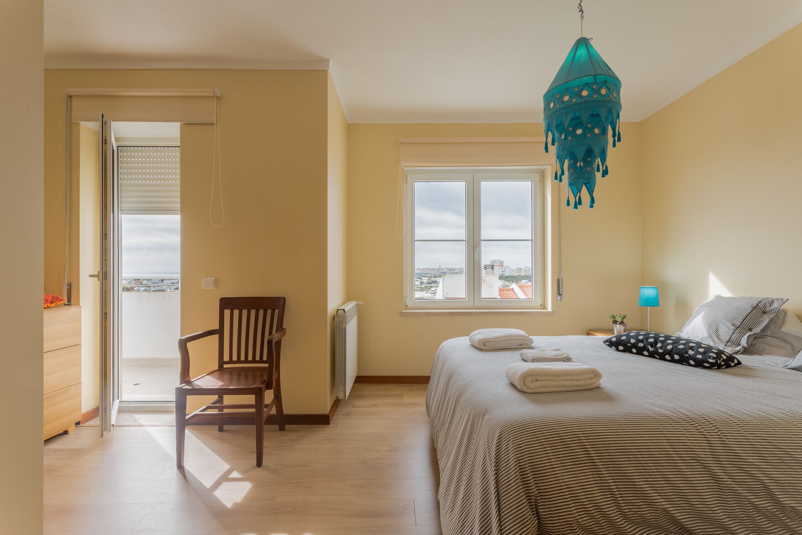 Ein Schlafzimmer mit Bett, Stuhl, Fenster und einer Pendelleuchte.