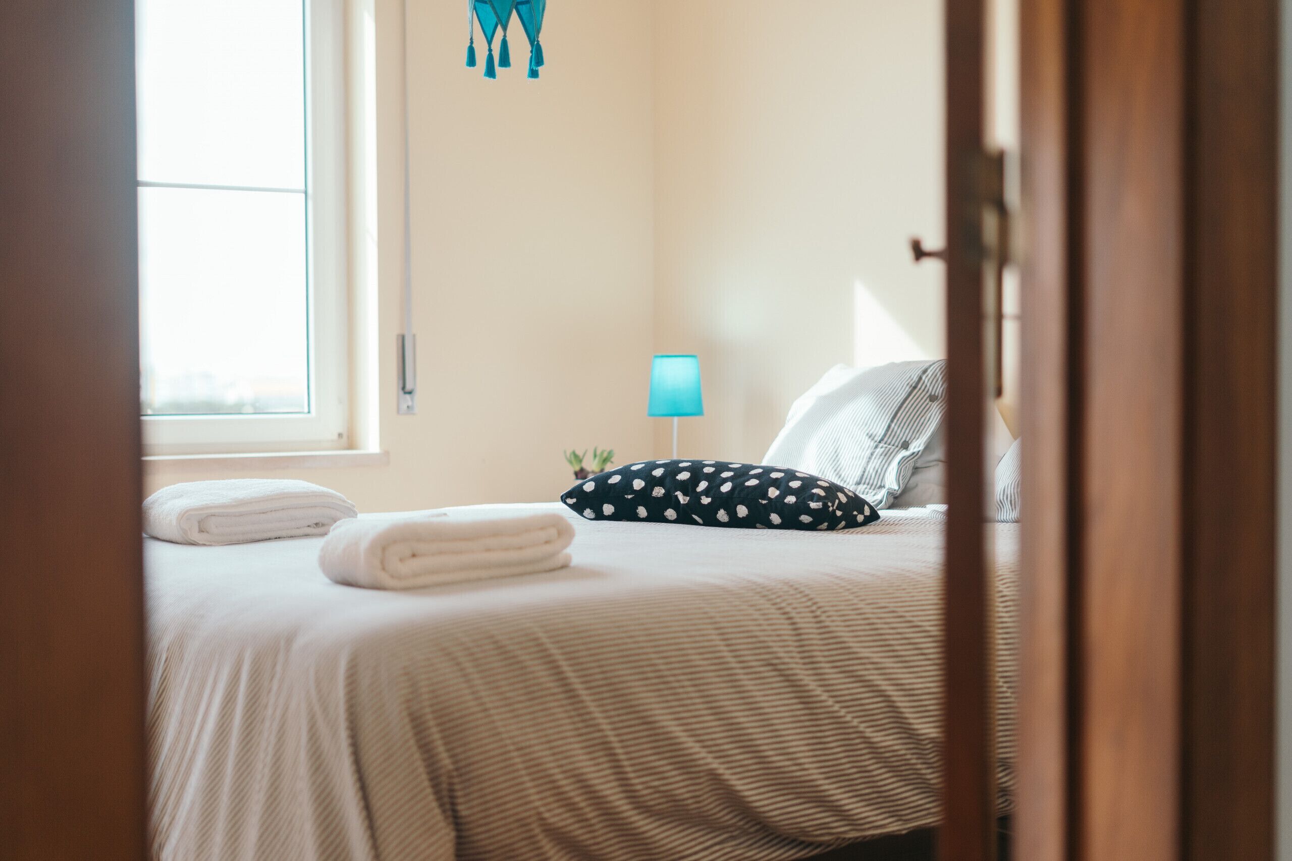 Un dormitorio con cama, ventana, lámpara y puerta.