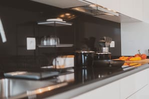 A modern kitchen with a black countertop, stainless steel appliances, and a wooden cutting board with vegetables. - Best Houses 25 - Seaside Retreat (Consolação)