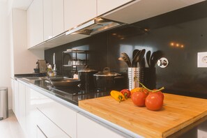 A modern kitchen with white cabinets, a black countertop, and a wooden cutting board with tomatoes and peppers. - Best Houses 25 - Seaside Retreat (Consolação)