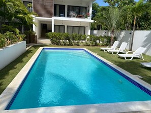 A rectangular swimming pool with a blue tiled edge, surrounded by white lounge chairs and a well-maintained lawn. - Charming 1-bedroom apartment with AC in Las Terrenas - LAS BAELLENAS (Las Terrenas)