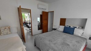 Een slaapkamer met een groot bed, een kleiner bed, een spiegel en een deur naar een badkamer.