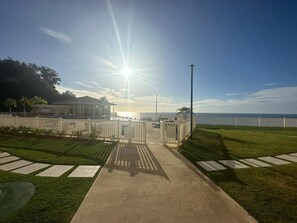 En stig som leder fram till en byggnad med utsikt över havet, ett vitt staket och en klar himmel.