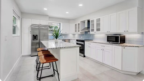 A modern kitchen with white cabinets, a granite countertop, a stainless steel refrigerator, and a microwave. - Delray Beach Paradise - Downtown Atlantic Ave (Delray Beach)