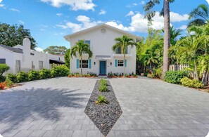 A white building with a central entrance, surrounded by a paved driveway and tropical landscaping. - Delray Beach Paradise - Downtown Atlantic Ave (Delray Beach)