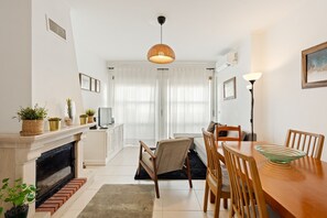 Ein modernes Wohnzimmer mit Kamin, Essbereich und großem Fenster mit durchsichtigen Vorhängen.
