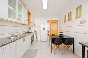 A compact kitchen with a sink, stove, and refrigerator, a dining table with chairs, and a door leading to another room. - Best Houses 36 - Baleal Surf Village (Baleal)