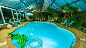 Uma piscina interior com teto de vidro, rodeada por cadeiras e guarda-sóis.