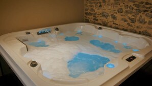 Ofurô com jatos de água, painel de controle e parede de pedra ao fundo.