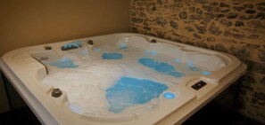 A hot tub with water jets, a control panel, and a stone wall in the background.