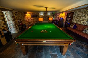 A pool table in a room with stone walls, a ceiling fan, and a bar area with bookshelves.
