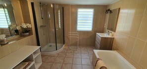 A modern bathroom with a glass shower enclosure, a bathtub, a sink, and a window with blinds. - Gîtes Holiday home in Normandy SPA Swimming pool and games room (Canisy)