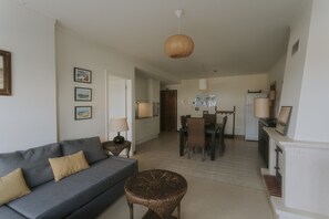 A living room with a sofa, a round wicker table, and a dining area with chairs and a table. - Best Houses 40 - You me and the sea (Baleal)