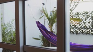 Vista a través de una ventana con una planta en maceta, un tejido púrpura colgante y una valla enrejada.