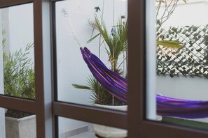 A view through a window with a potted plant, a hanging purple fabric, and a lattice fence. - Best Houses 40 - You me and the sea (Baleal)