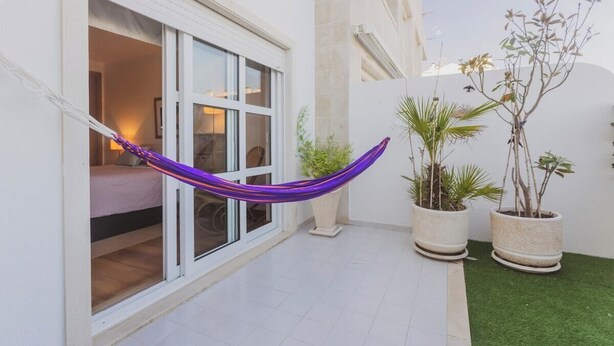 Un edificio blanco con puerta corredera de vidrio, una hamaca y plantas en macetas.