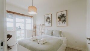 Un dormitorio con una cama, dos cuadros enmarcados, una ventana y una lámpara colgante.