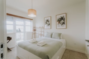 A bedroom with a bed, two framed pictures, a window, and a hanging light fixture. - Best Houses 40 - You me and the sea (Baleal)