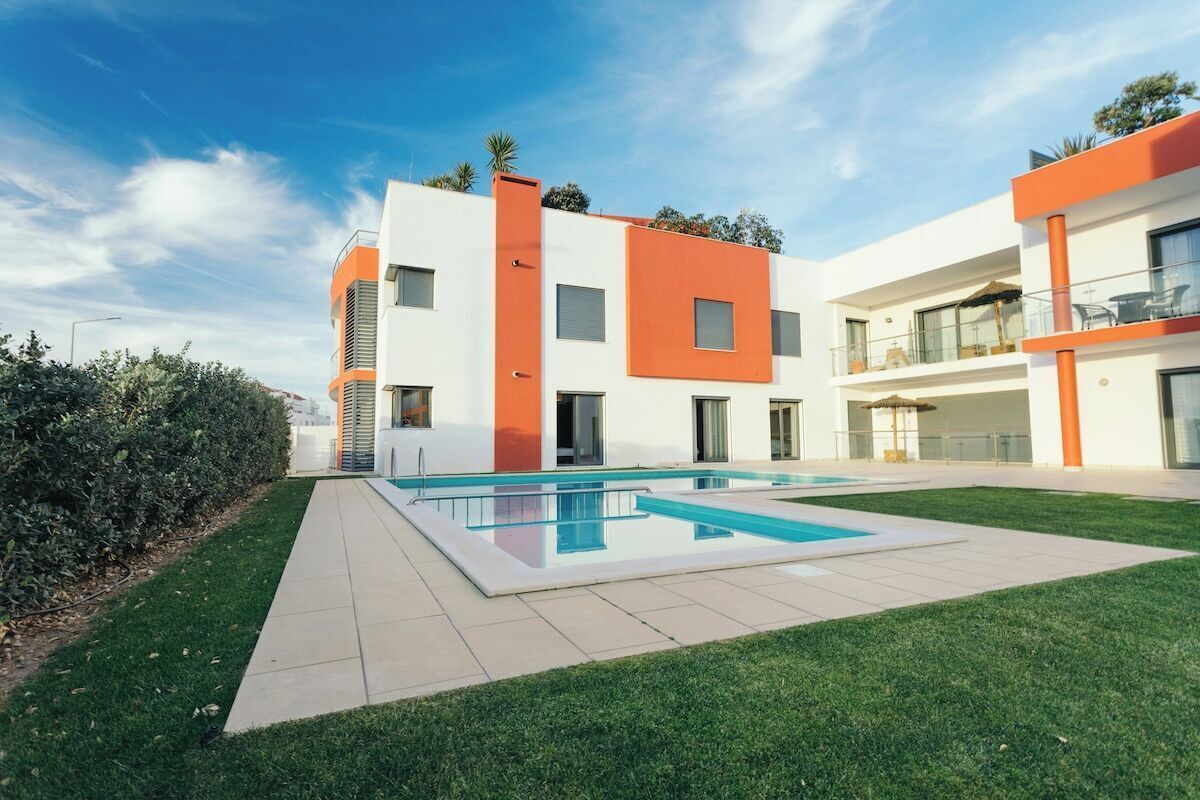A modern two-story building with a swimming pool, a well-maintained lawn, and a clear blue sky.