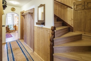 Eine Holztreppe mit Geländer, ein Wandspiegel und eine Tür mit Kleiderhaken.
