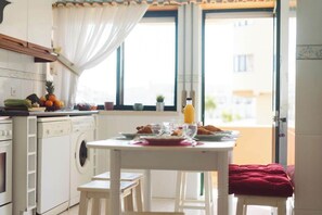 A kitchen with a washing machine, a dining table set with plates, glasses, and a bottle. - Best Houses 18 - Typical Portuguese Apartament (Consolação)