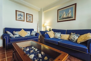 A living room with two blue sofas, a coffee table with seashells, framed pictures on the walls, and a lamp. - Best Houses 18 - Typical Portuguese Apartament (Consolação)